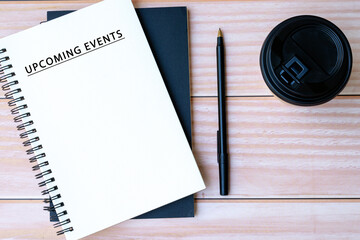 Upcoming events text on notepad with pen and disposable coffee cup a desk