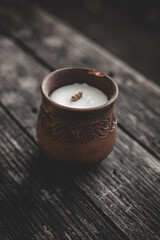 Candle in a brown clay pot on a wooden background