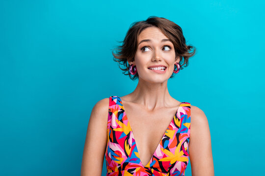 Photo of interested funny woman with bob hairdo dressed colorful clothes look empty space biting lips isolated on blue color background