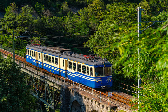 Historic electric train on famous steel bridge in Intragna in Centovalli valley. Narrow gauge railway line from Locarno to Domodossola in Italy in the Swiss Alps. Popular tourist train attraction.