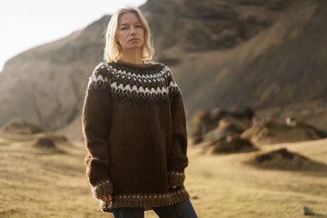 A girl in fashion clothes poses in mountains an Icelandic sweater