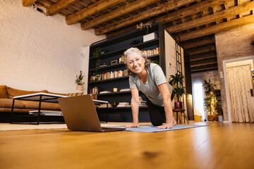 An active senior woman doing yoga following the steps in laptop. Senior woman in the living room of...