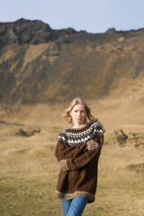 A girl in fashion clothes poses in mountains an Icelandic sweater