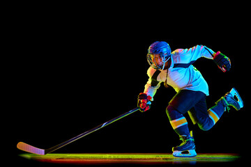 Dynamic image of young girl, hockey player in uniform and helmet, in motion with stick against...