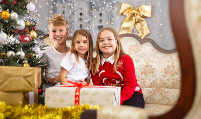 Fototapeta na wymiar Satisfied children rejoice with New Year gifts, sitting on the sofa next to New Year tree