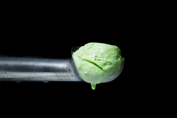 A metal spoon with a melting pistachio ice cream scoop dripping drops from it. Isolated on a black...