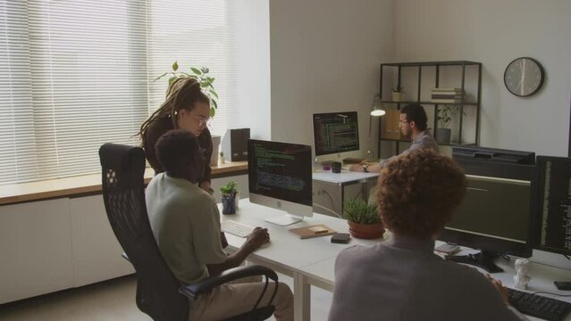 Back view shot of multiracial colleagues looking at html code on computer screen and having discussion, working with other software engineers in modern programmers office