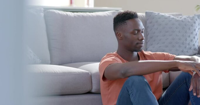 Worried african american man sitting and thinking in sunny living room, slow motion