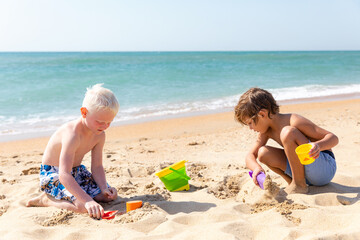 Children two little boys playing on the beach on summer holidays. Children having fun with a sand on the seashore. Vacation concept. Happy sunny day. Joyful children with beautiful sea, sand