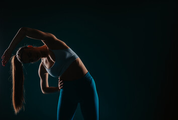 Confident woman showcasing body transformation through exercise in a dark studio. Muscular silhouette, fit physique, strong muscles. Fitness model inspiring others.