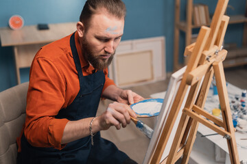 Talented artist in home studio. Creative artist sitting in front of drawing easel and painting