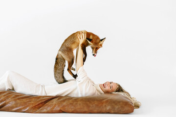 A girl in a white pullover, and black hat  holds a red fox in her hands. The blonde in studio. Pretty woman with fox on white background.