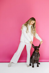 Young woman with her cute drathaar in armchair in studio on pink background. Lovely pet..Girl with blonde hair holding dog breed german wirehaired pointer drathaar