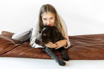 Young woman with her cute drathaar in armchair in studio on white background. Lovely pet..Girl with blonde hair holding dog breed german wirehaired pointer drathaar