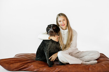 Young woman with her cute drathaar in armchair in studio on white background. Lovely pet..Girl with blonde hair holding dog breed german wirehaired pointer drathaar