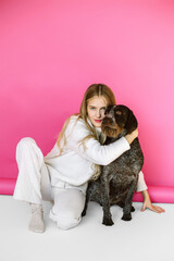 Young woman with her cute drathaar in armchair in studio on pink background. Lovely pet..Girl with blonde hair holding dog breed german wirehaired pointer drathaar