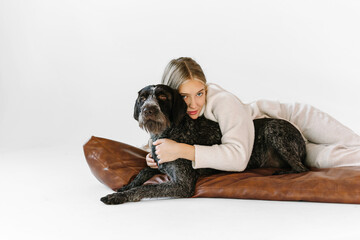 Young woman with her cute drathaar in armchair in studio on white background. Lovely pet..Girl with blonde hair holding dog breed german wirehaired pointer drathaar