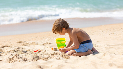 Happy child little boy playing with the sand on the beach, building sand castle, enjoying summer,...