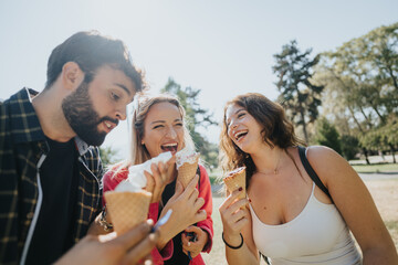 Carefree friends, laughing and enjoying a sunny day in a city park. With positive energy, they relax, socialize, and indulge in ice cream, creating lasting memories in the green environment of nature.