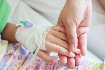 Mother holding child hand with saline IV solution in hospital