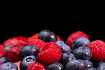 Colorful berries close-up on a black background, front view, macro photography. Blueberries, raspberries, strawberries. Concept of healthy nutrition