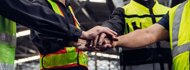 Team engineers and foreman stack hand and shake hands to show success at factory machines....