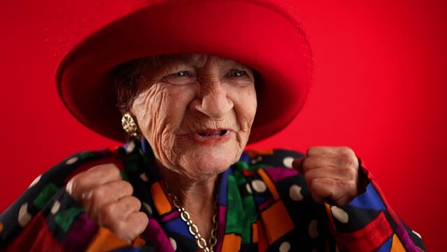 Slow motion angry unhappy displeased fisheye portrait caricature of funny elderly woman saying NO with red hat isolated on red background.