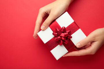 White gift with red bow in female hands on red background. Space for text.