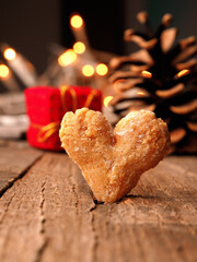 Close up of a tasty heart shaped cookie on a rustic wooden table, blurred Christmas lights and gift boxes in the background
