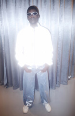 Full length fashion portrait of young Black man wearing 90s style light reflective jacket and...