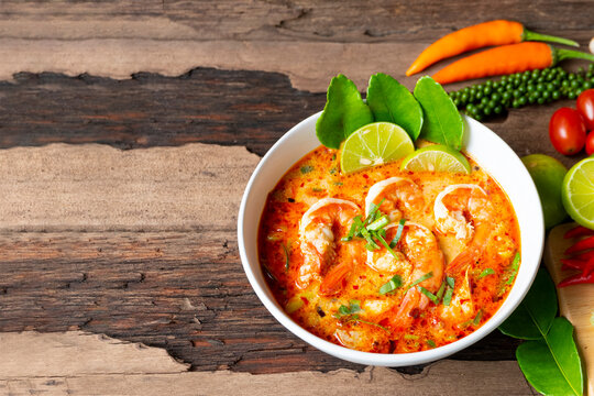Tom Yum Goong or Shrimp soup spicy sour Soup Traditional food in Thailand contains chili, lime,lemongrass, lime leaf, along with cooked rice in a white dish on the old wood background from top view.