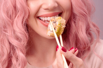 Young woman with red nails and pink hair is eating sushi.