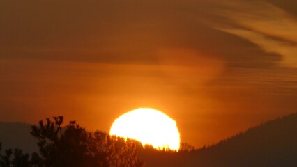 Orange sky and yellow sunrise over dark horizon of mountains with forests. Sun disc with...