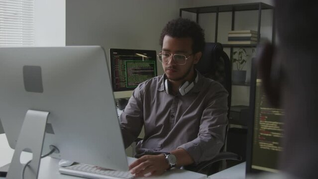 Waist up of young Biracial man working on computer in open space office, coding and developing new software
