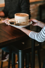 Waitress serving a man at a restaurant table with a plate featuring two small sauce containers and a larger wooden bowl of gyozas