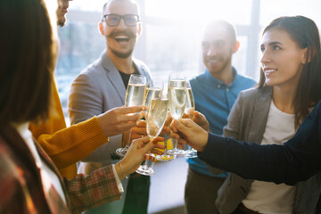 Colleagues in the office celebrate the concluded deal with champagne and sparkling wine. A group of people with glasses of champagne having fun, relaxing in the office. Concept of work, holiday. - obrazy, fototapety, plakaty