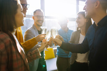 Colleagues in the office celebrate the concluded deal with champagne and sparkling wine. A group of people with glasses of champagne having fun, relaxing in the office. Concept of work, holiday. - obrazy, fototapety, plakaty