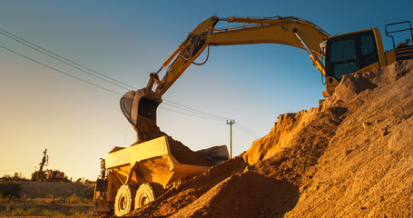 Construction Site On Sunny Evening: Industrial Excavator Loading Sand Into A Truck. The Process Of...