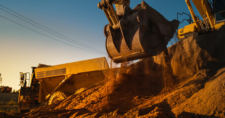 Construction Site On Sunny Evening: Industrial Excavator Loading Sand Into A Truck. The Process Of...