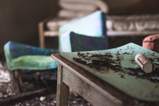 Decaying table, forgotten in an abandoned house, accompanied by a worn sofa chair, embodying echoes of a past life