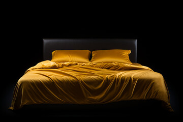 Bed with yellow comforter and pillows on it in dark room. - obrazy, fototapety, plakaty