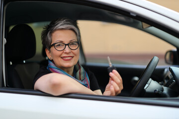 A happy Caucasian woman sitting in a car, smiling and holding the steering wheel, portraying joy and a love for driving.