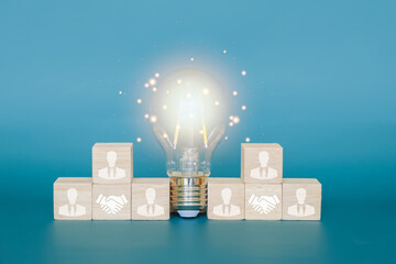 Teamwork concept, businessman icon on a wooden block and a glowing light bulb in the middle,...