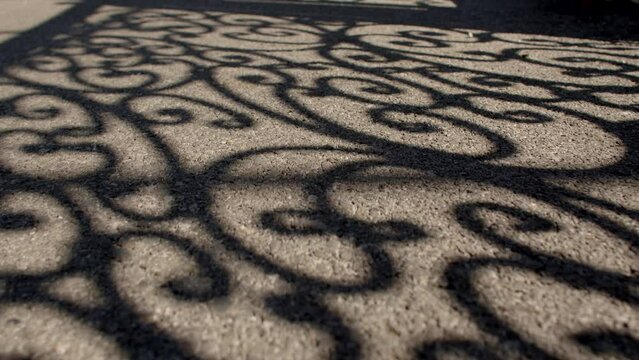 Shadows on the sunlit asphalt from an intricately carved beautiful fence symbolize abstract or hidden beauty that is not always evident on the surface.