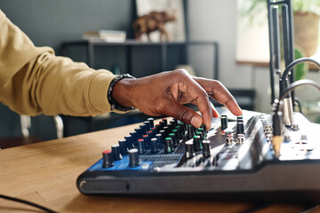 Hand of young male host turning consoles on soundboard and adjusting sounds while preparing for...