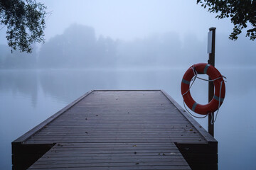 Wooden pier in the blue morning mist, with a life preserver ring