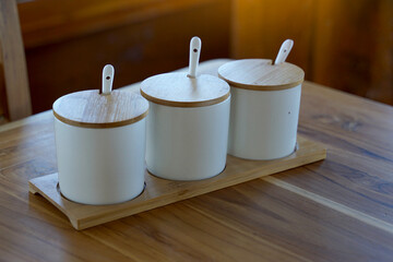 Set of ceramic cups with lids made from wood placed on thedining table for adding condiments such...
