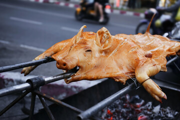 Crispy pig grilled on spit traditional coal and fire. A whole pig roasted on an open fire. Asian or oriental street food or festive food.