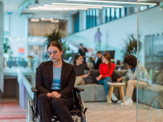 In a modern office, a young businesswoman in a wheelchair is surrounded by her supportive...