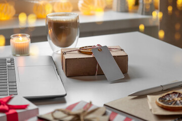 Notepad with a pen, laptop, coffee cup, wrapped gifts on a desk table. Winter Festive atmospheric mood. Preparation for Christmas. Business Holidays Concept. Freelancer's desktop during Xmas vacation